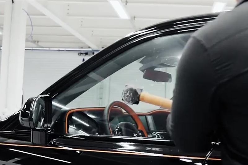 Teste de impacto: uma marreta golpeia o vidro lateral de um carro preto no estúdio da Évora Maxx